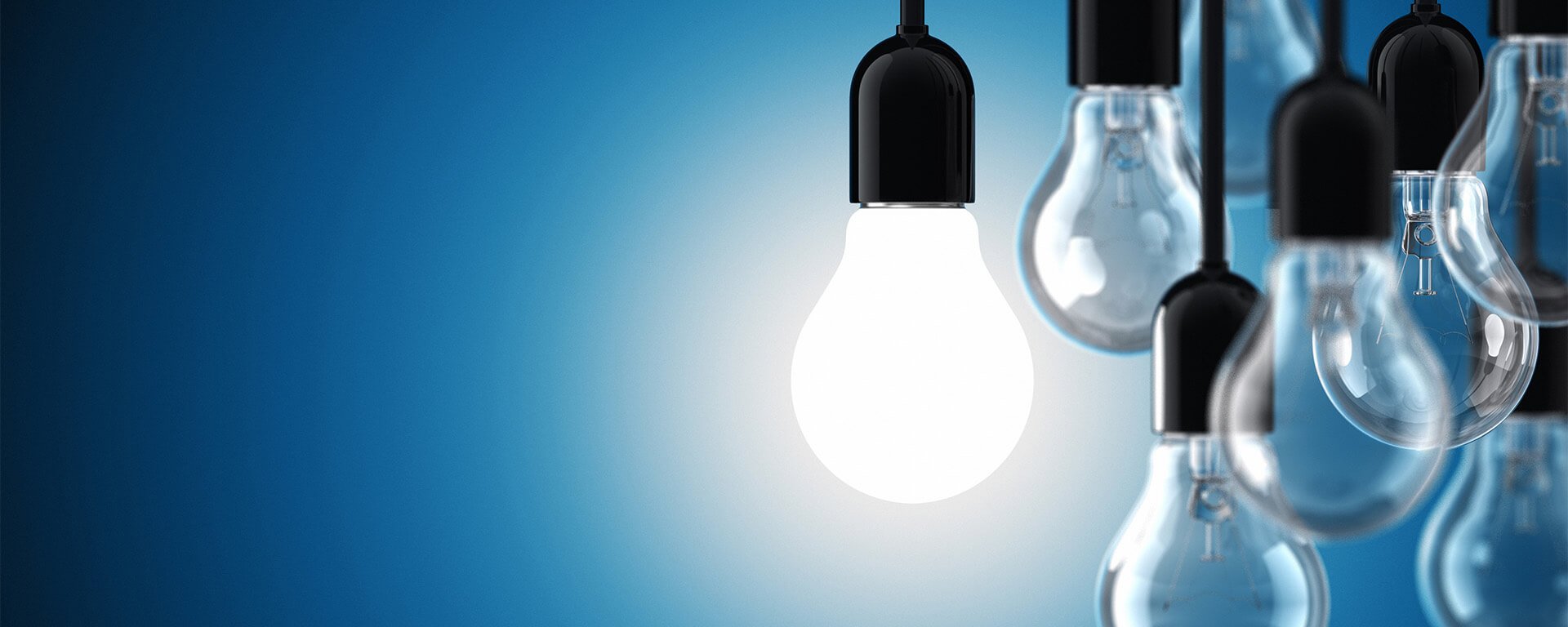 A group of hanging lightbulbs with a single bulb illuminated against a blue background
